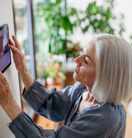 Mature,Woman,Adjusting,Smart,Thermostat,,Touch,Screen,Of,Smart,Home